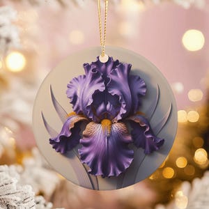 May include: A circular ceramic ornament depicting a detailed purple iris flower with yellow and brown highlights. The flower is set against a light grey background, with a gold string for hanging. The ornament is designed for decorative purposes.
