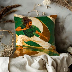 Op de afbeelding: Een vierkant sierkussen met een bedrukte illustratie van een persoon met dreadlocks in een vechtsport-houding. De persoon draagt een donkergroen t-shirt en een wijde witte broek. De achtergrond bestaat uit abstracte groene en gouden gebogen vormen.