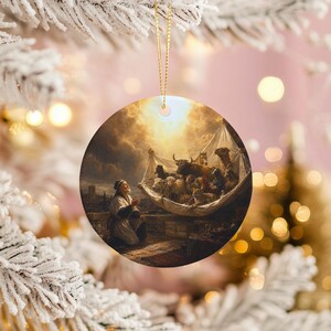 以下が含まれることがあります： 宗教画が描かれた丸いセラミック製のクリスマスオーナメント。 祈りを捧げる男性と、明るい光に照らされたハンモックのような構造の中にいる動物が描かれています。 オーナメントは金の紐で吊るされています。