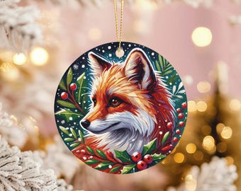 Peut inclure: Ornement de Noël rond avec une illustration détaillée d'une tête de renard. Le renard a une fourrure orange et blanche, entourée de feuilles vertes, de baies rouges et d'un fond enneigé. Une ficelle dorée est attachée pour l'accrocher.