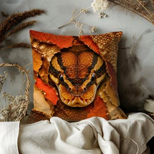 Peut inclure: Coussin carré décoratif avec une image détaillée d'une tête de serpent. Le serpent présente des marques marron, noires et jaunes. Le coussin a un design déchiré et texturé avec des accents orange et dorés, créant un effet 3D.