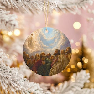 Puede incluir: Adorno navideño redondo con una pintura religiosa de una figura ascendiendo al cielo, rodeada por un grupo de personas mirando hacia arriba. El adorno tiene una cuerda dorada para colgar y un fondo borroso de árbol de Navidad.
