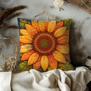 May include: Square decorative pillow featuring a large, detailed sunflower design. The pillow has a vibrant color palette of yellow, orange, and green, with a dark blue border. The sunflower's center is a mix of red and green.