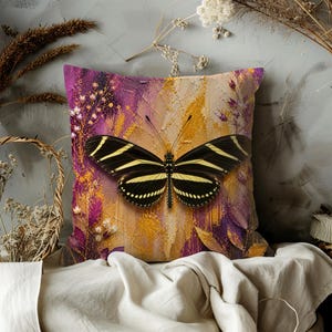 May include: Square decorative pillow featuring a large butterfly with black and yellow striped wings. The pillow has a purple and gold abstract background with floral accents. The pillow is likely made of a soft fabric.