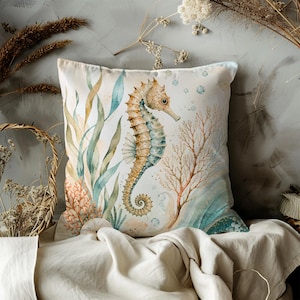 May include: Square cushion with a watercolour seahorse design. The seahorse is tan and teal, surrounded by aquatic plants and coral in shades of green, orange, and brown. The cushion has a neutral background.