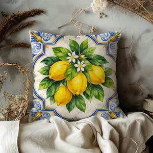 May include: Square decorative pillow featuring a watercolor illustration of lemons, green leaves, and white flowers. The design is framed by a blue and yellow border, creating a vibrant and fresh aesthetic. The pillow is likely made of a soft fabric.