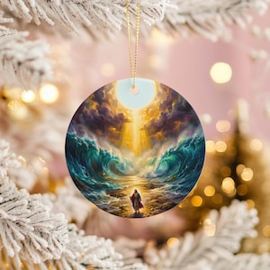 May include: Round Christmas ornament featuring a dramatic painting of a figure standing between towering ocean waves, with a bright light shining through the clouds. The ornament has a gold string for hanging.