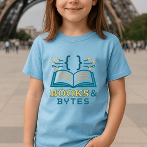May include: A light blue t-shirt featuring a graphic design with the text "BOOKS & BYTES". The design includes an open book, curly brackets, and circuit-like elements in teal and yellow. The shirt is worn by a person.