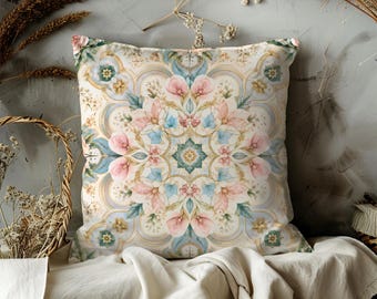 May include: Square decorative pillow with a floral mandala design. The pillow features a cream background with a symmetrical pattern of pink, blue, and green flowers. The pillow is likely made of a soft fabric and is designed for home decor.