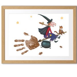 以下が含まれることがあります： 額縁に入った、ほうきに乗った魔女と猫のイラスト。魔女は黒い帽子とマント、赤いトップス、青いスカートを着ています。ほうきは手形です。背景は白で、星と葉が描かれています。