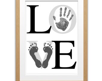 May include: Framed art print with the word "LOVE" in black letters. The "O" is a gray circle with a handprint inside. The "V" is formed by two gray footprints. The frame is light brown.