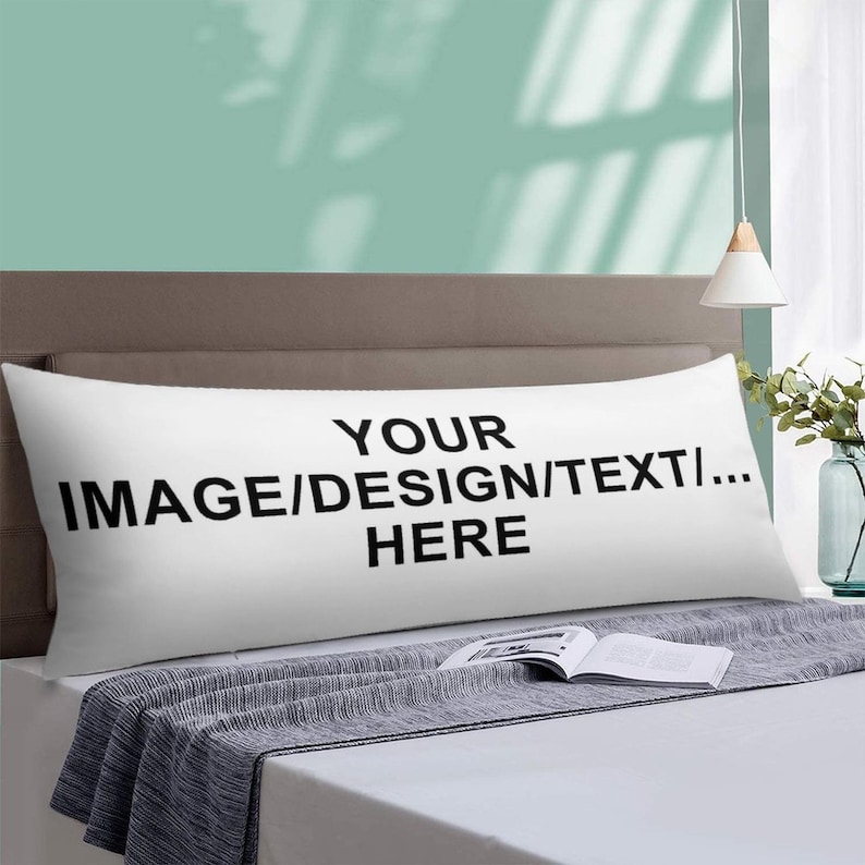 Może przedstawiać: Długa, biała poduszka do ciała z czarnym napisem "YOUR IMAGE/DESIGN/TEXT... HERE". Poduszka leży na ł&oacute;żku z szarym kocem i książką. Tło to jasnozielona ściana.