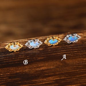 Könnte beinhalten: Vier kleine marquiseförmige Ohrstecker in einer Reihe angeordnet. Zwei Ohrringe haben goldfarbene Fassungen mit irisierenden blauen Steinen, während zwei silberfarbene Fassungen mit irisierenden blauen Steinen haben. Die Buchstaben A und B sind sichtbar.