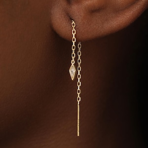 May include: A gold threader earring featuring a delicate chain design. The earring includes a small, marquise-shaped clear stone accent suspended on one side of the chain and a thin, straight gold bar at the end of the other chain segment.