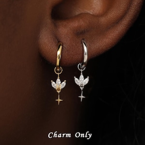 May include: Two small hoop earrings, one gold and one silver, each featuring a dangling charm shaped like a three-petaled flower with a small star point at the bottom. The charms are set with clear stones. The text Charm Only is visible.