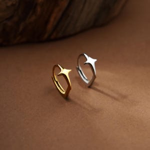 May include: Two hoop earrings, one in a polished gold tone and one in a polished silver tone, each featuring a prominent four-pointed star design centered on the hoop. The earrings are circular with a hinged closure mechanism visible on the side.