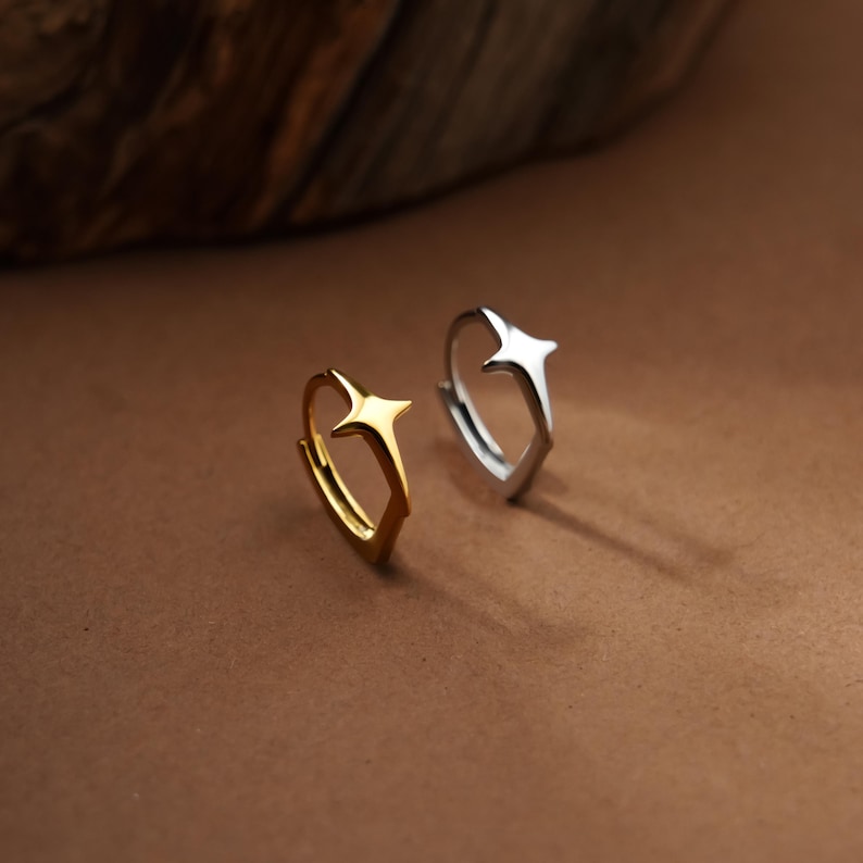 May include: Two hoop earrings, one in a polished gold tone and one in a polished silver tone, each featuring a prominent four-pointed star design centered on the hoop. The earrings are circular with a hinged closure mechanism visible on the side.