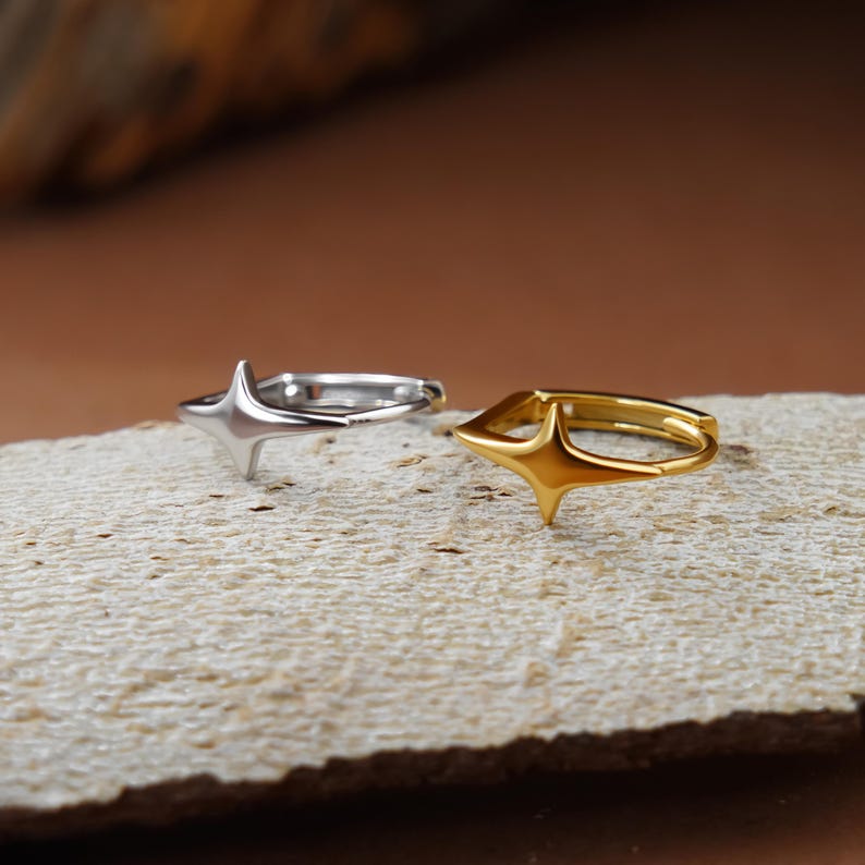 May include: Two hoop rings, one in a silver tone and one in a gold tone, each featuring a prominent four-pointed star design on the front. The rings are circular with a smooth, polished finish, showcasing a distinct star-shaped focal point.