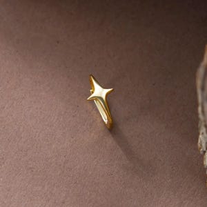 May include: A gold-toned hoop earring featuring a four-pointed star charm. The star has a smooth, polished surface with elongated, tapered points. The hoop is circular and connects to the base of the star, creating a cohesive metallic piece.