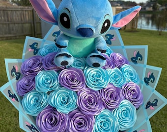 May include: A bouquet featuring a plush Stitch character atop a bed of blue and purple paper roses. The bouquet is wrapped in light blue paper with Stitch illustrations, creating a whimsical and colourful arrangement.