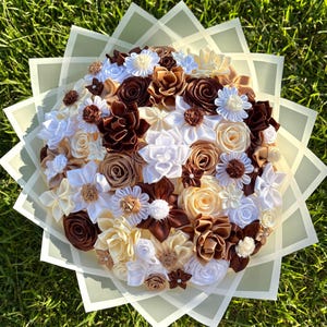 Peut inclure: Un bouquet fait à la main de fleurs en tissu dans les tons de blanc, crème, marron et beige. Les fleurs sont disposées en cercle et enveloppées dans du papier vert clair. Le bouquet est posé sur un fond d'herbe verte.