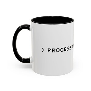 May include: A white ceramic mug with a black handle and a black interior. The exterior features the black pixelated text > PROCESSING. The mug has a cylindrical shape with a curved handle on the left side, designed for holding hot or cold beverages.