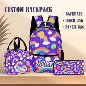 May include: A purple backpack, lunch bag, and pencil bag set with a rainbow and balloon pattern. The backpack has black straps and a front pocket. The lunch bag has black handles. The pencil bag is rectangular. The name "Brian" is printed on each bag.