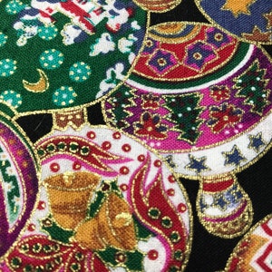 May include: A black fabric with a repeating pattern of colorful Christmas ornaments. The ornaments are decorated with gold, silver, and red accents. The fabric is perfect for crafting projects, such as making holiday decorations or sewing festive clothing.