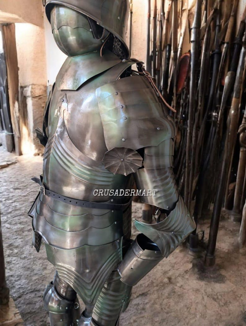 May include: A full suit of medieval armor, crafted from polished metal with a greenish hue. The armor includes a helmet, chest plate, shoulder guards, and arm and leg protection. The image shows the armor from the back, with the text "CRUSADERMART" visible.