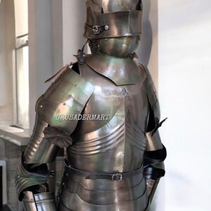 May include: A full suit of medieval armor made of polished metal. The armor includes a helmet, chest plate, shoulder guards, arm and leg protection, and a belt. The armor is designed to protect the wearer from injury in battle.