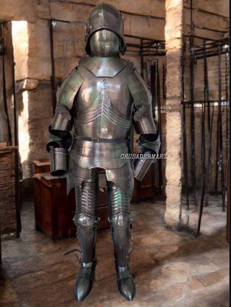 May include: Full suit of medieval armor made of polished steel. The armor includes a helmet, chest plate, arm and leg protection, and is displayed in a stone room. The text "CRUSADERMART" is visible on the armor.