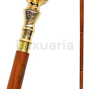 Könnte beinhalten: Dekorative Gehstock mit einem goldfarbenen, verzierten Griff und einem dunkelbraunen Holzschaft. Der Griff weist florale und schildartige Designs auf. Ein klassisches Accessoire.