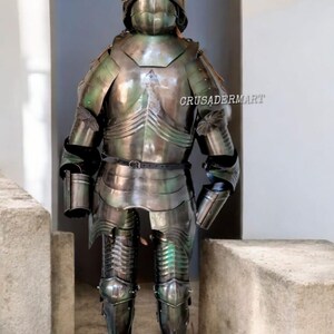 May include: Full suit of medieval armor, featuring a helmet, chest plate, and leg guards. The armor is made of polished metal with a reflective surface, showing hints of green and silver. The text "CRUSADERMART" is visible on the armor.