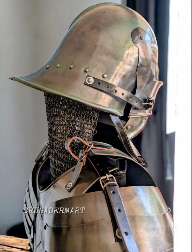 May include: A medieval-style metal helmet and chest armor set. The helmet has a wide brim and is riveted. The chest armor is secured with leather straps. A chainmail collar is visible. The text "CRUSADERMART" is printed on the chest armor.