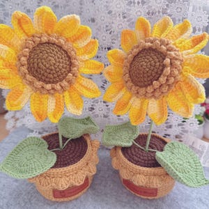 Può includere: Due girasoli all'uncinetto fatti a mano in vaso. I girasoli hanno petali gialli e arancioni con centri marroni. I vasi sono beige con "terra" marrone e foglie verdi. Ogni vaso ha una piccola etichetta marrone.