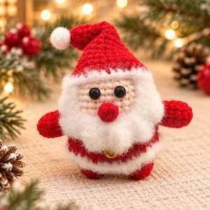 Könnte beinhalten: Eine kleine, handgehäkelte Weihnachtsmann-Figur mit einer roten Mütze und weißem Bommel, einem beigen Gesicht mit schwarzen Perlenaugen, einer roten Nase und einem flauschigen weißen Bart. Der Körper ist rot mit weißem Saum und einer kleinen Goldglocke.