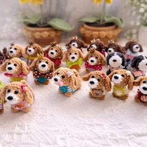 Peut inclure: Une collection de figurines de chiens au crochet faites à la main. Les chiens ont des fourrures marron et blanches, certains portant des couronnes, des nœuds et des tenues colorées. L'arrière-plan comprend des plantes en pot et une surface blanche texturée.
