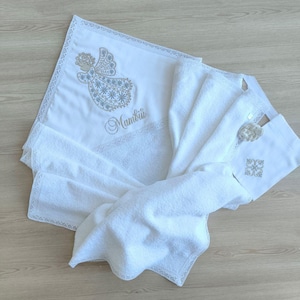 May include: White baby blanket with a white embroidered angel and the name "Mambiii" on it. The blanket has a lace trim.