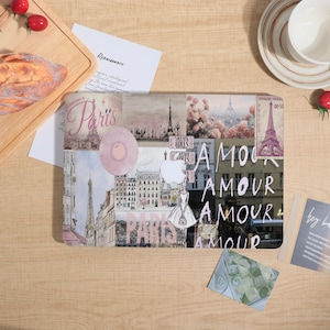 May include: A laptop skin featuring a collage of Paris-themed imagery, including the Eiffel Tower, pink flowers, and architectural sketches. The design incorporates the text Paris and Amour in various fonts, alongside a silhouette of a person.