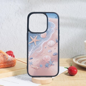 Pode incluir: Uma capa de telemóvel com um design de praia. A capa tem uma borda preta e uma ilustração colorida de uma praia arenosa com conchas, estrelas do mar e ondas do oceano. A paleta de cores inclui tons de rosa, azul e branco.