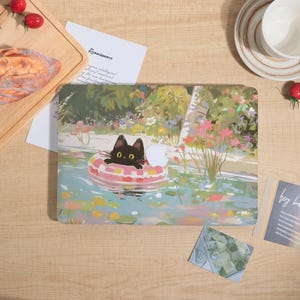 Könnte beinhalten: Eine Laptop-Hülle mit einer Illustration einer schwarzen Katze, die in einem rosa-weißen Schwimmring in einem Teich schwimmt. Der Hintergrund zeigt eine Gartenszene mit Blumen und Grün. Die Hülle hat ein weißes Apple-Logo.