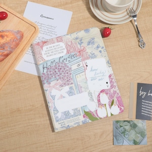 Pode incluir: Uma bolsa decorativa com zíper com um design de colagem com elementos florais e arquitetônicos. A bolsa tem uma etiqueta retangular branca com o texto "how lucky are we". O texto adicional inclui "Hello Gorgeous" e "Isaías 40:8".