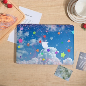 May include: A laptop skin featuring a blue sky with white clouds and a scattering of colorful stars in shades of pink, orange, green, and yellow. The design includes a central white Apple logo cutout against the celestial background.