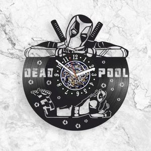 May include: A circular wall clock crafted from a black vinyl record featuring a graphic of the character Deadpool. The design includes the text DEAD POOL, white clock hands, and a central gear mechanism. The character is shown in two poses.