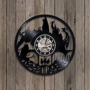 May include: A circular wall clock crafted from a black vinyl record featuring a laser-cut silhouette of a castle, an owl, and three figures. The center displays a white clock face with black numerals and hands, and the letters HP at the bottom.