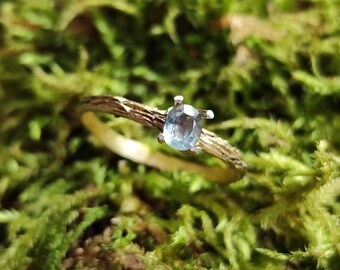 May include: A gold ring with a light blue gemstone set in a twig-like band.