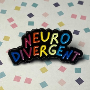 Peut inclure: Épingle en émail noir avec l'inscription "NEURO DIVERGENT" en couleurs arc-en-ciel. L'épingle a un contour noir et est posée sur un fond de losanges multicolores.