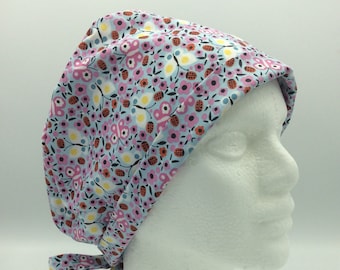 May include: A light blue scrub cap with a pink, white, and orange floral pattern. The cap has a tie at the back.