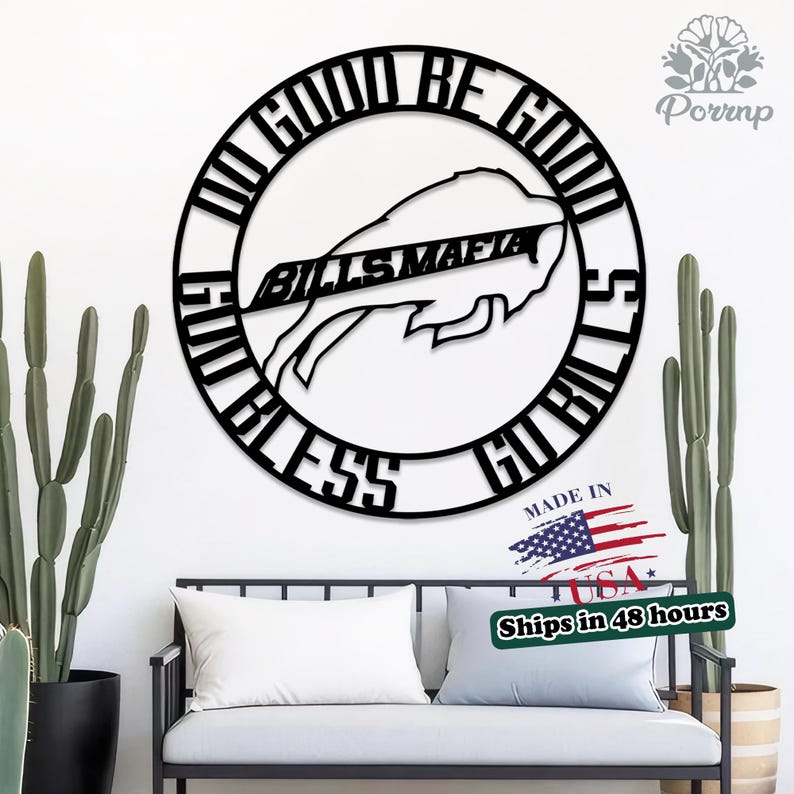 May include: Black metal wall art featuring the words "DO GOOD BE GOOD GO BILLS BLESS" encircling a buffalo logo with "BILLS MAFIA" inscribed. The artwork is displayed on a white wall, with cacti and a bench in the foreground.