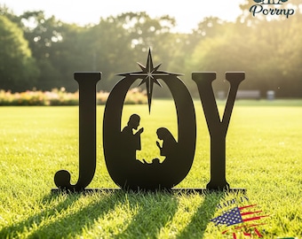 May include: Black metal sign spelling "JOY" with a nativity scene inside the "O" and a star above. The sign is placed on a grassy lawn with sunlight in the background. The sign has the text "Made in USA" and "Ships in 48 hours".